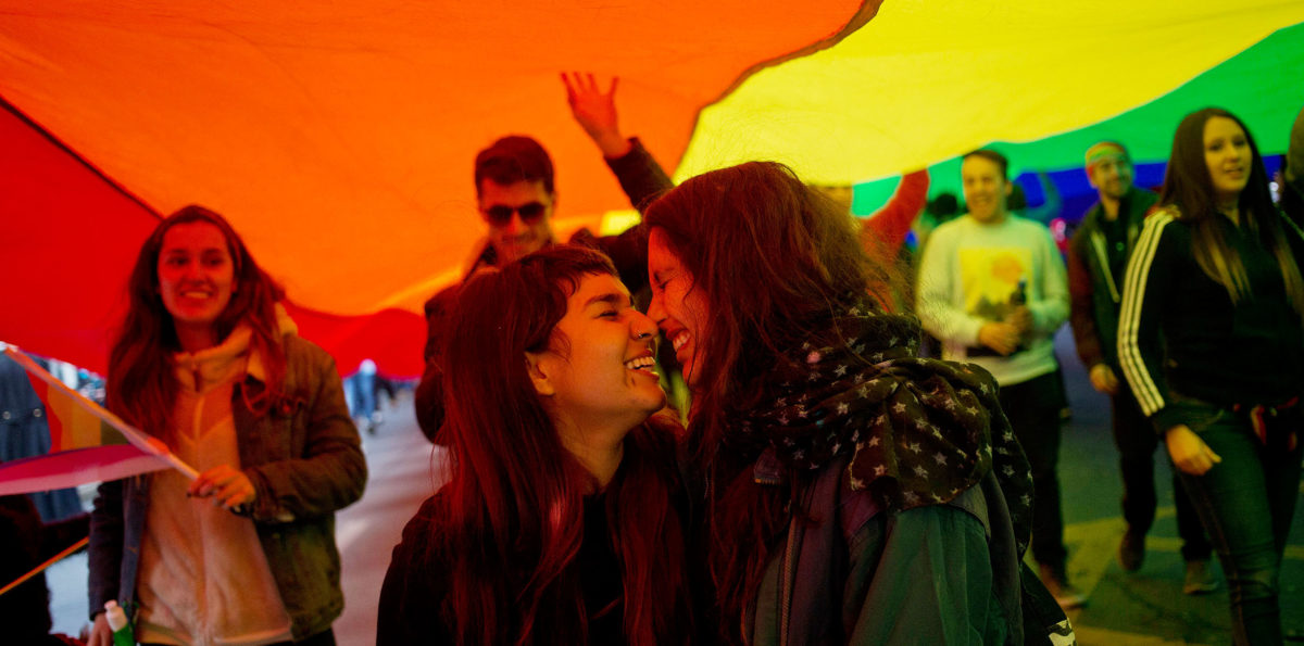 Mulheres se beijando durante evento LGBT no Chile, sob uma bandeira do arco-íris